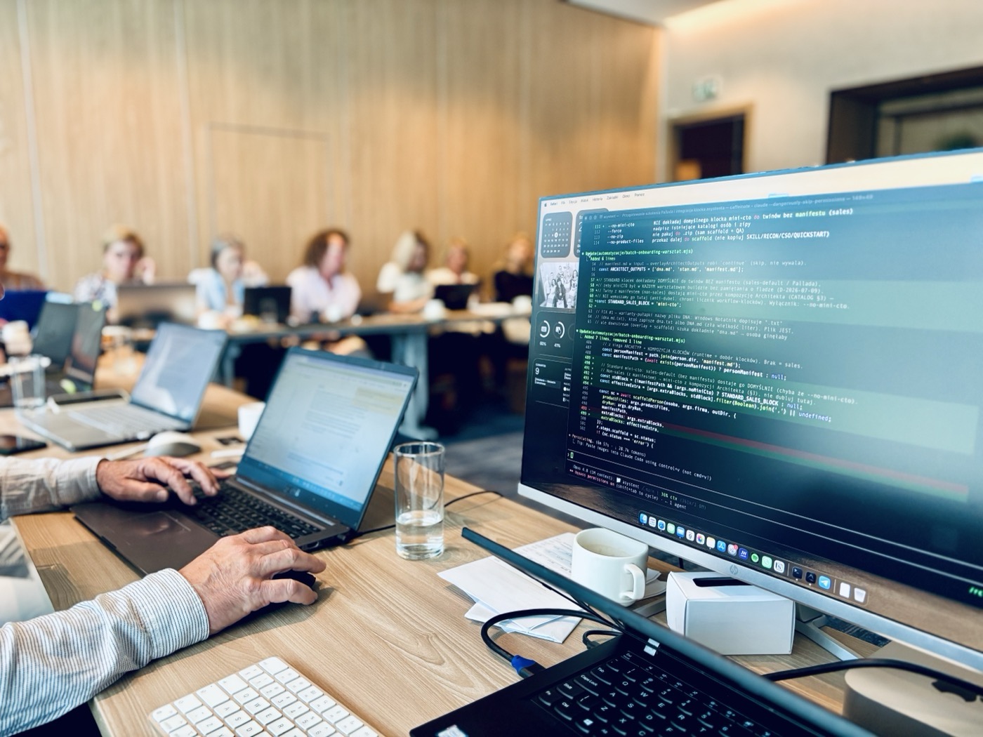 Sala warsztatowa: uczestnicy przy laptopach budują swoich asystentów AI, na pierwszym planie ekran prowadzącego z narzędziem warsztatowym